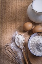 Aerial view copyspace composition pitcher with milk flour in bowl and spoon eggs corolla on wooden