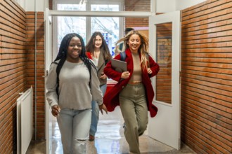 Happy multiethnic students running through a university hallway, celebrating friendship and