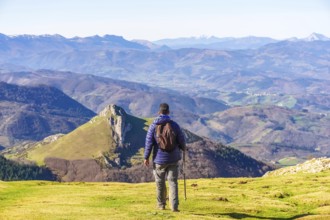 Hiker with backpack and trekking poles enjoying breathtaking mountain view from mount txindoki in