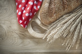 Bread chopping board wheat ears red tablecloth on wooden background