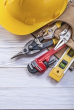 Composition of construction tooling in leather tool belt building helmet on wooden board