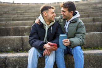 Two men sharing a tender moment, embracing on steps while holding coffee and a phone, enjoying each