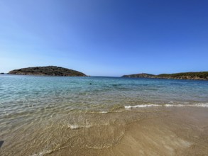 Calm beach with gentle waves and hills in the background under a blue sky, cagliari, sardinia,