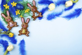 Easter bunny with colourful eggs, blue feathers and flowers on a light blue background