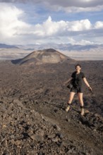 Smiling woman standing in front of a volcano in a vast landscape, Argentina, volcanoes, lava field,