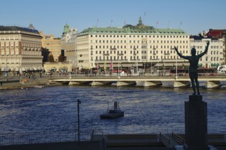 Statue near water and bridge with historical buildings in the background, Stockholm city centre,