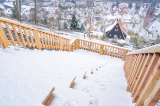 Snow-covered steps lead down to a picturesque village view in winter, New wooden footbridge in Calw