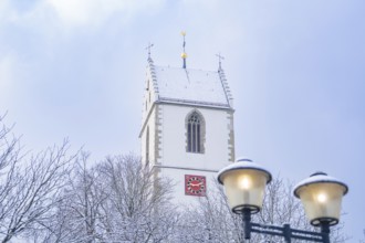 Church tower covered with snow, in front of a cloudy sky, accompanied by a street lamp, Aidlingen,