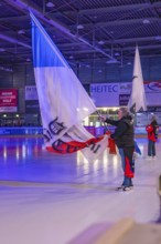 People waving large flags on an illuminated ice rink during an event, Heilbronner Falken Vs