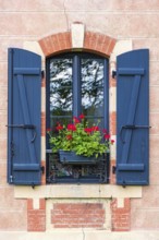 Window with shutters and red flowers in a window box on an old idyllic house, Bretagne, France,