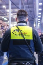 Rear view of a security guard in a yellow waistcoat in an arena full of spectators, Heilbronner