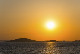 Small sailing boats on calm sea in orange sunset next to island, view from island Murter, Dalmatia,