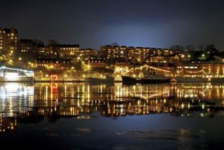 Night city view with illuminated slopes, ships and reflections, winter, ice, capital, Södermalm,