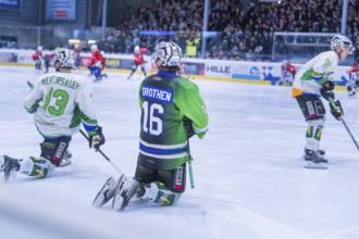 Two ice hockey players in green jerseys kneeling on the ice during a game in front of an audience,