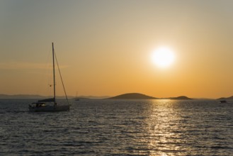 Sailboat on calm sea at sunset with golden yellow sky, view from island Murter, Dalmatia, Croatia,