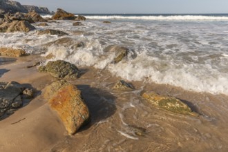 A rocky beach with a large rock in the foreground and a boat in the distance. The beach is quiet