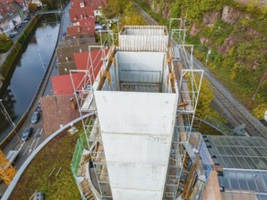 Construction site of a concrete tower next to a river with surrounding red houses and autumn trees,