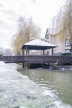 Wooden bridge over a snow-covered river in front of residential buildings, Aidlingen, Böblingen