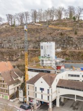 Construction site with crane and buildings in front of an autumnal hill and railway tracks,