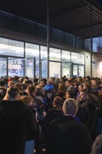 People waiting in a long queue at the entrance of an illuminated sports arena, Heilbronner Falken