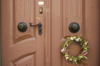 Detail of an antiquated front door with floral wreath and no advertising sign in a building on the