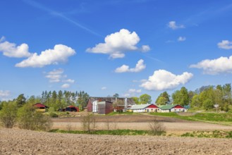 Farm with barns by field with bare soil on a sunny spring day in the Swedish countryside, Sweden,