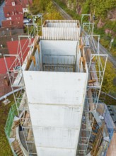 Concrete tower with scaffolding in the middle of red house roofs and autumn landscape from above,