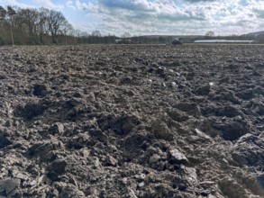 Freshly ploughed field in spring, tractor with plough in the background, Germany, Europe