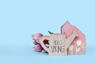 Seasonal decor arrangement with house, pink tulip flowers and watering can with text 'Hello spring'