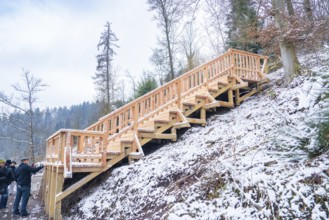 Snow-covered wooden stairs in the winter forest, with people nearby, New wooden footbridge in Calw