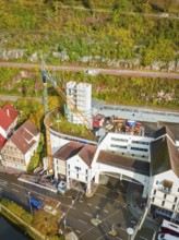 Construction site with crane and buildings surrounded by green hills and streets, extension of the