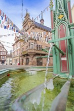 Historic town centre with green fountain and colourful pennants in front of an old building,