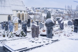 Snow-covered cemetery with numerous gravestones near a church, Aidlingen, Böblingen district,