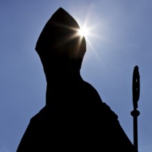 Anonymous Catholic bishop with mitre and crozier as a silhouette against the light, symbolic photo