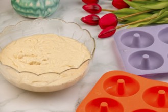 Dough placed next to baking moulds for donuts, red tulips in the background