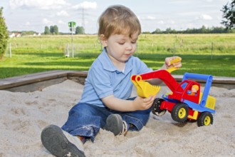 Three-year-old boy on the playground, sitting in the sandpit and playing with an excavator, toy,