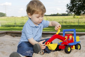 Three-year-old boy on the playground, sitting in the sandpit and playing with an excavator, toy,