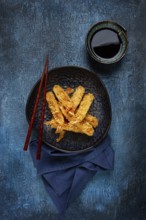 Shrimp in tempura, deep fried, on a black plate, with soy sauce, close-up, top view, no people