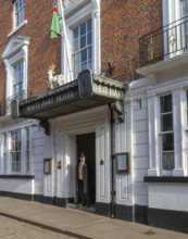 Doorman standing in entrance door of historic White Hart Hotel, Bailgate, city of Lincoln,