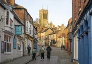 People walking up Steep Hill in evening light, cathedral tower rising above buildings, Lincoln,