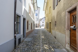 Narrow pavement of old buildings, accompanied by shadows of building facades and shutters,