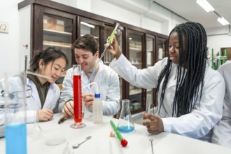 Multi ethnic university students wearing lab coats conducting a chemistry experiment using colorful