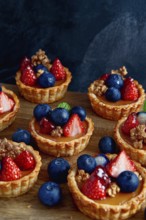 These miniature fruit tarts, adorned with fresh blueberries and vibrant strawberries, sit on a