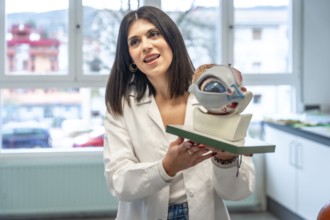 Young woman wearing lab coat holding anatomical model of eye and optic nerve, explaining its