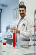 Young male scientist pouring blue liquid into laboratory glassware while smiling during an