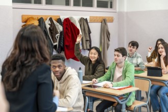 Multi ethnic group of high school students attending a lesson, a girl is raising her hand to ask a