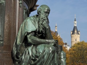 Bronze statue of a pensive man in front of a historic castle on an autumn day, Schwerin, Germany,