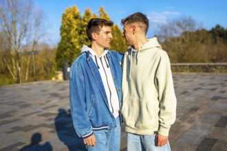 Two men embracing and smiling in a public park, sharing a joyful romantic moment together under the