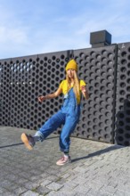 Urban dancer performing a street dance move outdoors, wearing a yellow beanie and blue denim