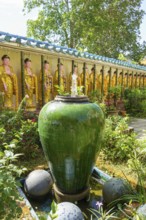 Garden with large ceramic pot, plants and Buddha figures along a wall, penang, malaysia